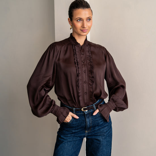 Woman wearing brown shirt and jeans posing with her hands in her pockets
