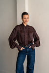 Woman wearing brown shirt and jeans posing with her hands in her pockets