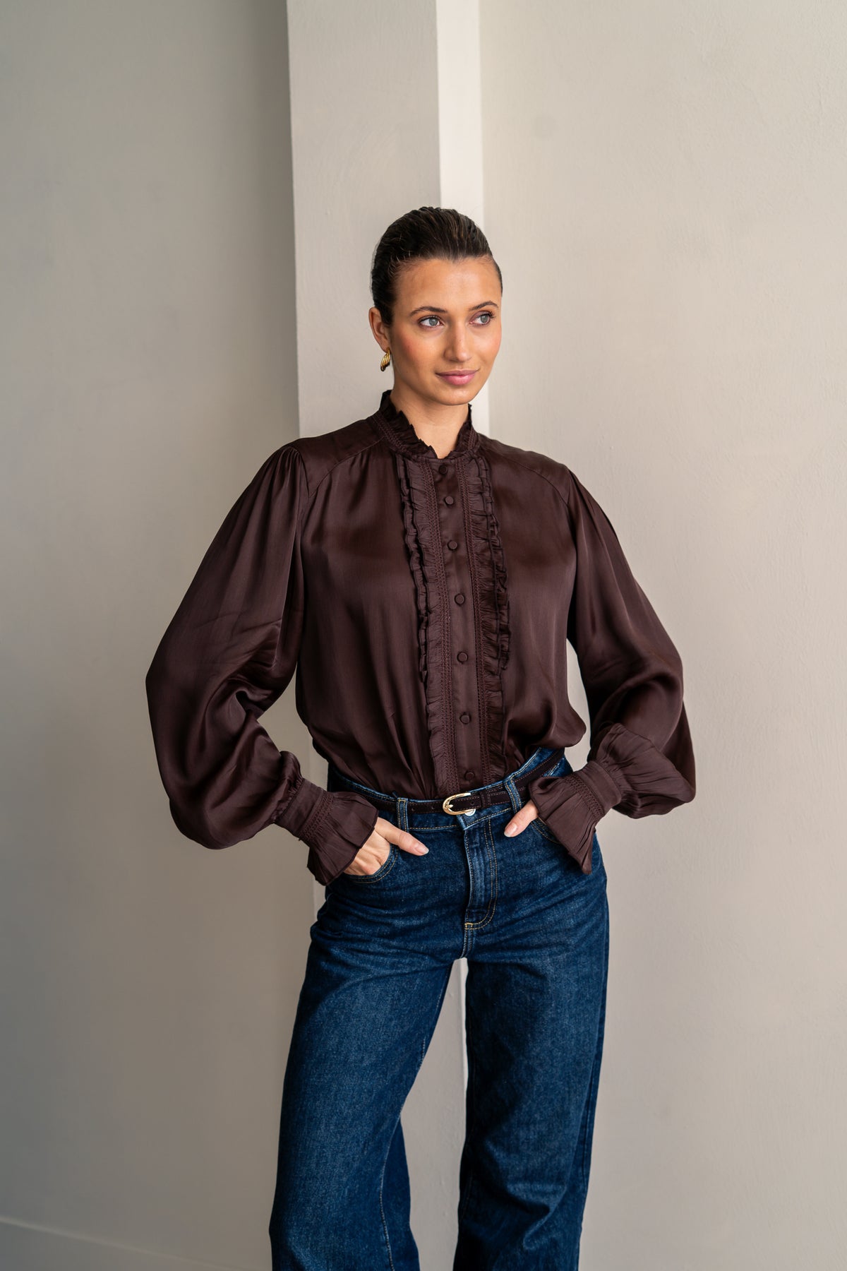Woman wearing brown shirt and jeans posing with her hands in her pockets