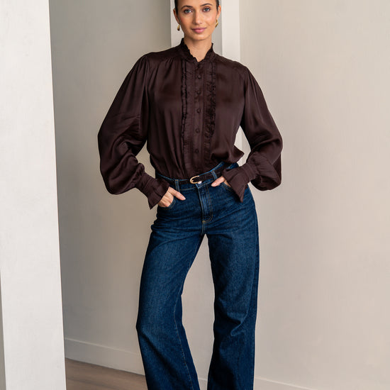 Woman wearing a brown blouse and jeans looking into the camera