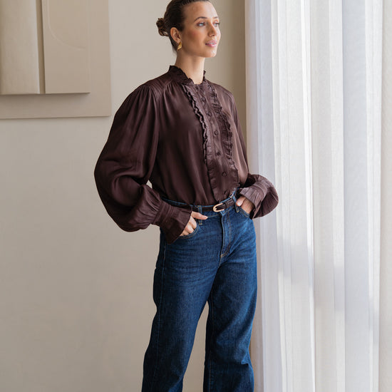 woman wearing brown blouse with blue jeans looking out of window