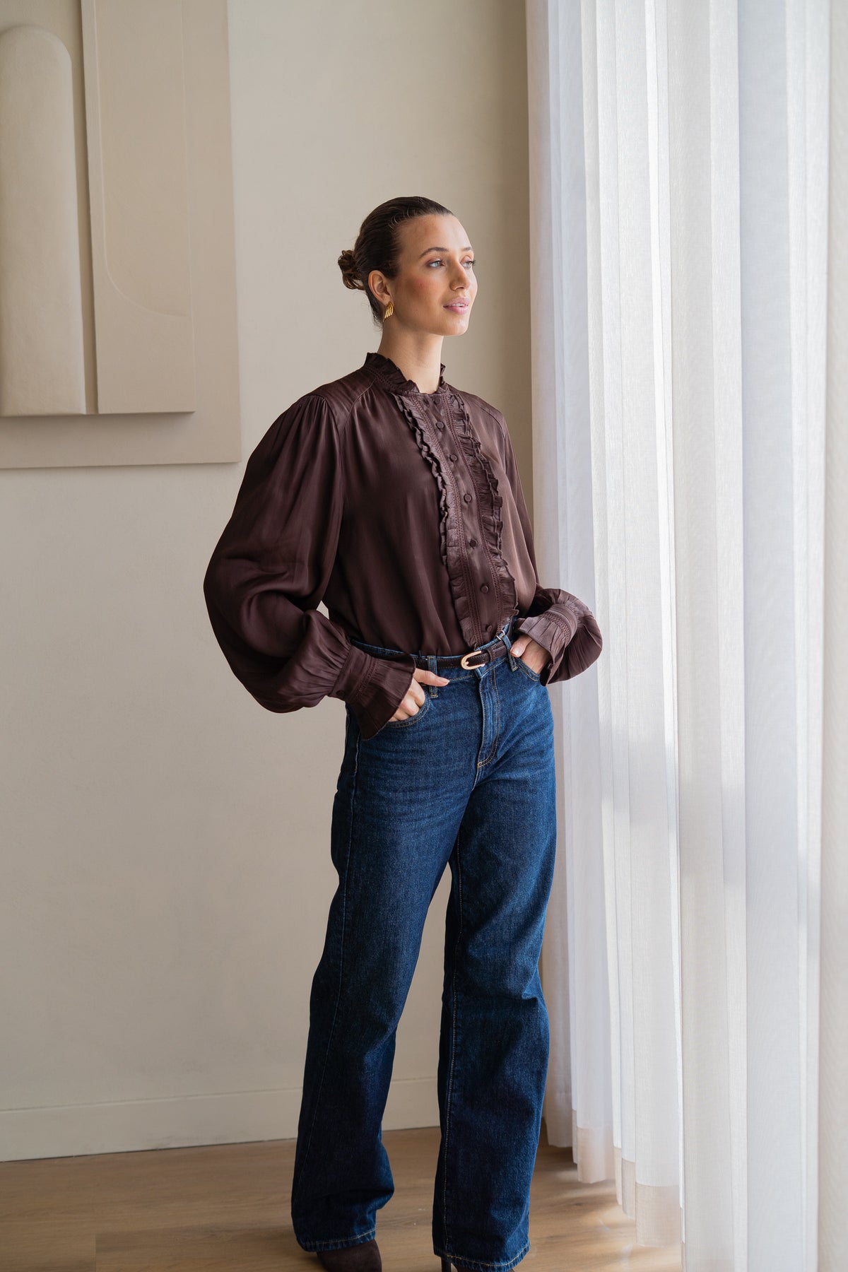woman wearing brown blouse with blue jeans looking out of window