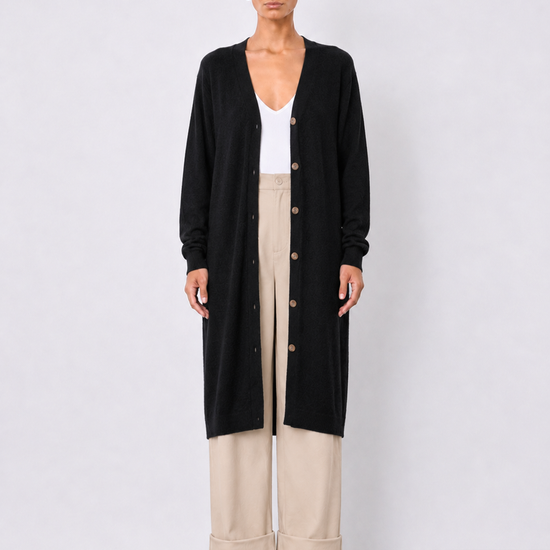 A model stands against a light gray studio background wearing a long black cardigan over a white top and beige wide-leg cropped pants.