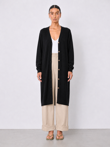 A model stands against a light gray studio background wearing a long black cardigan over a white top and beige wide-leg cropped pants.