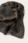 A dark charcoal gray scarf with a warm brown abstract pattern and the brand name 'ba&sh' woven into it, shown on a light beige background.