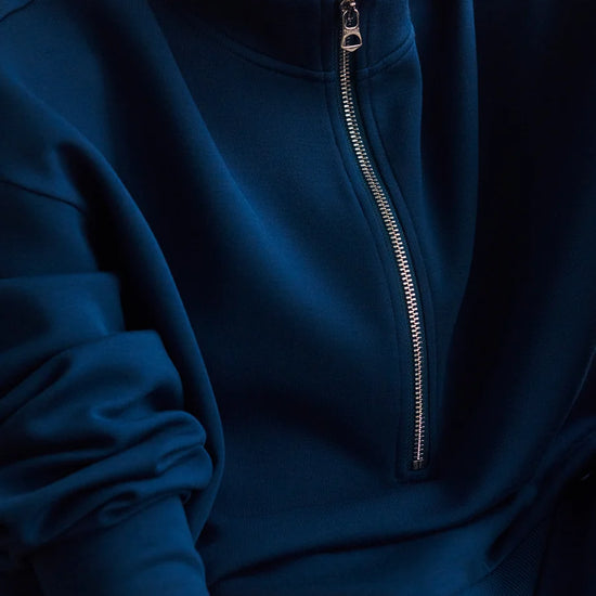 A close-up of a person wearing a dark blue half-zip sweatshirt, showing the silver zipper and ribbed fabric details.