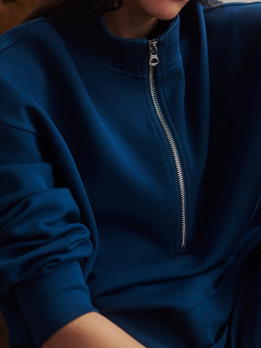 A close-up of a person wearing a dark blue half-zip sweatshirt, showing the silver zipper and ribbed fabric details.