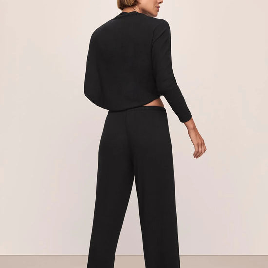 Woman wearing a black outfit with wide-leg pants against a plain background