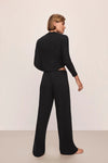 Woman wearing a black outfit with wide-leg pants against a plain background
