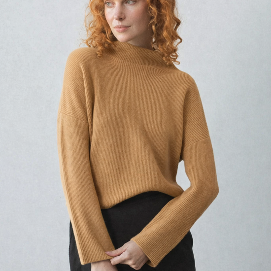 Woman wearing a camel colour cashmere sweater against a plain background