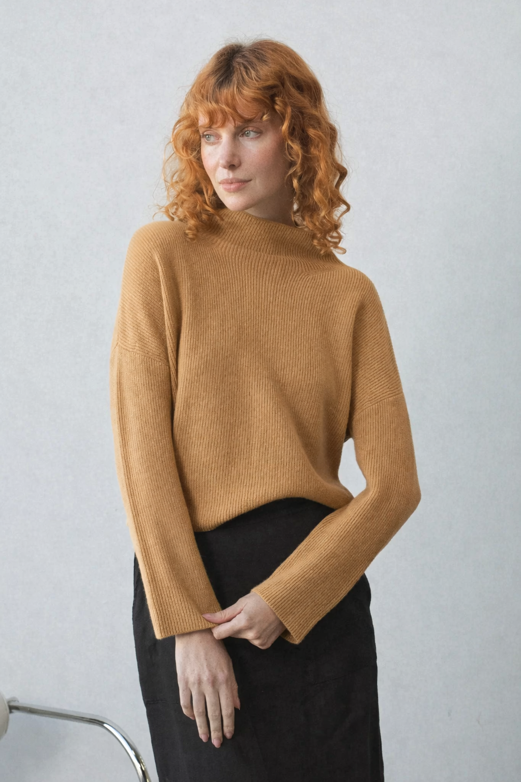 Woman wearing a camel colour cashmere sweater against a plain background