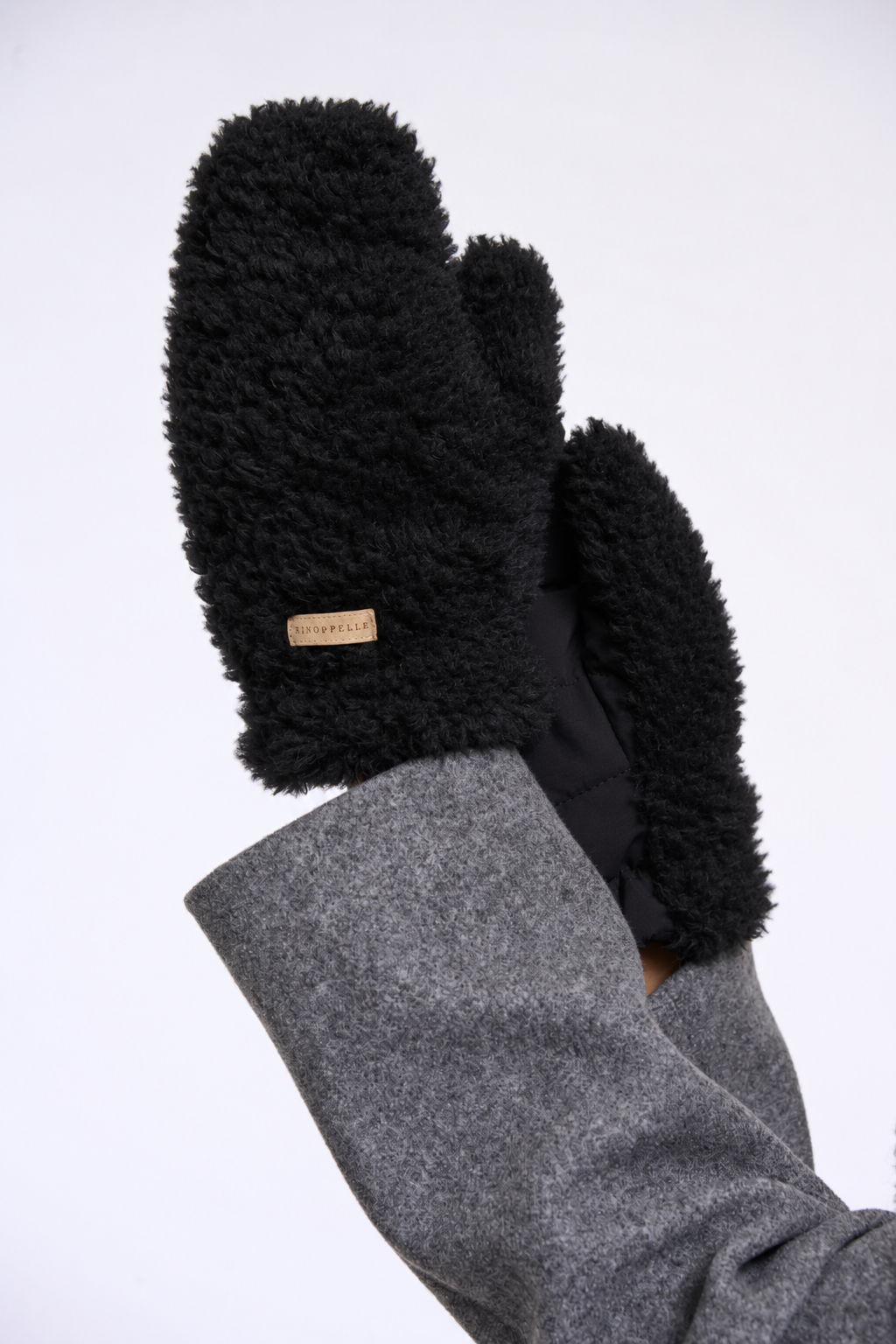 Black fleece-lined mittens worn on hands, shown against a plain white background. The sleeves are gray, and a small tan brand tag is visible on one mitten.