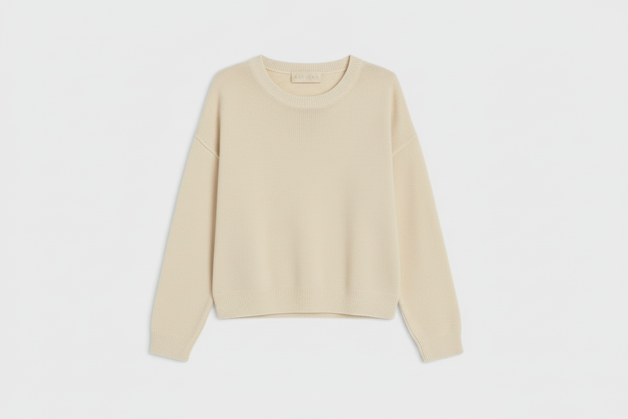 A light beige knit crewneck sweater with long sleeves, laid flat against a light gray background.