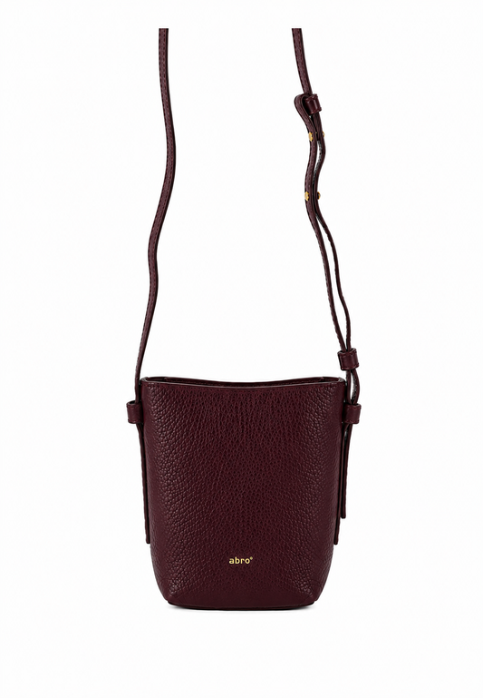 A dark burgundy pebbled leather crossbody bag with a thin matching leather strap and a small gold logo on the front, shown against a plain white background.