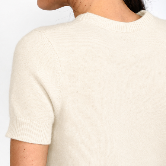 Close-up back view of a person wearing a short-sleeve cream knit sweater against a plain white background.