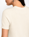 Close-up back view of a person wearing a short-sleeve cream knit sweater against a plain white background.
