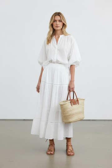 Woman in a white outfit holding a straw bag against a plain background