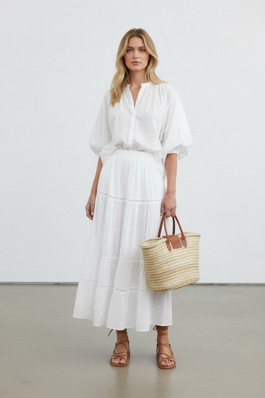 Woman in a white outfit holding a straw bag against a plain background