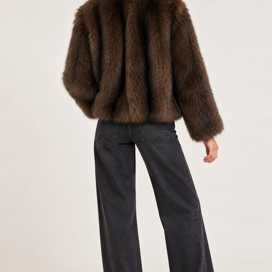A model shown from the back wearing a cropped brown fur jacket and dark charcoal wide-leg jeans against a plain light background.