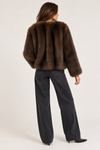 A model shown from the back wearing a cropped brown fur jacket and dark charcoal wide-leg jeans against a plain light background.