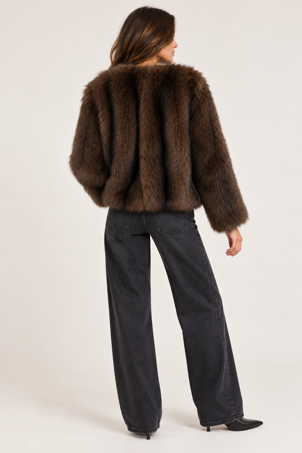 A model shown from the back wearing a cropped brown fur jacket and dark charcoal wide-leg jeans against a plain light background.
