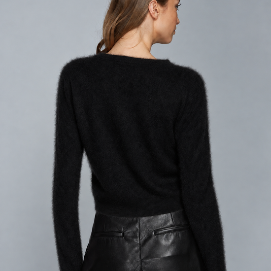 A woman shown from the back wearing a black fuzzy long-sleeve sweater and black leather pants against a plain gray studio background.