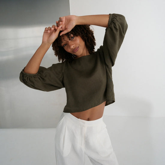 Woman wearing a green cropped top and white pants against a plain background