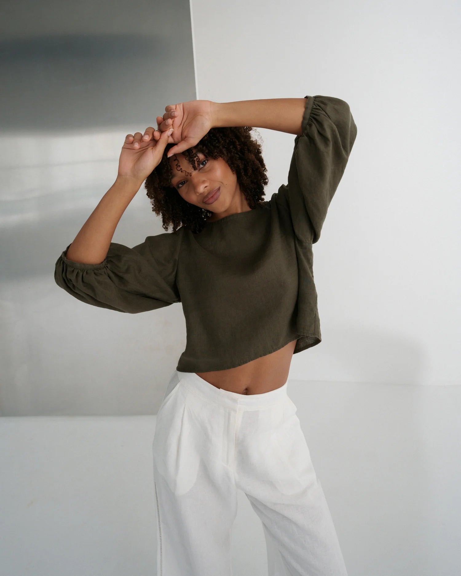Woman wearing a green cropped top and white pants against a plain background