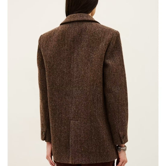 A person shown from the back wearing an oversized brown textured blazer with dark brown pants, photographed against a plain light beige studio background.