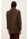 A person shown from the back wearing an oversized brown textured blazer with dark brown pants, photographed against a plain light beige studio background.