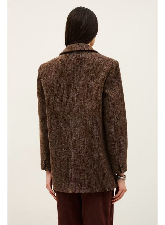 A person shown from the back wearing an oversized brown textured blazer with dark brown pants, photographed against a plain light beige studio background.