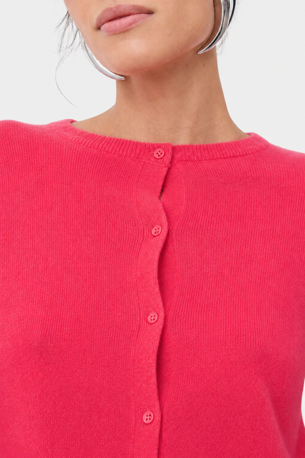 Close-up of a model wearing a bright pink ribbed knit cardigan sweater with a button-up front.