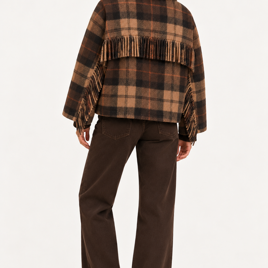 A woman shown from the back wearing a brown and tan plaid fringed cape jacket with dark brown wide-leg pants and black boots, against a plain white studio background.