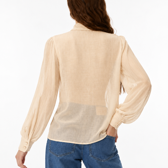 A woman shown from the back wearing a light beige long-sleeve blouse and blue jeans against a plain white studio background.