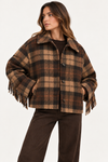 A woman wearing a brown and tan plaid fringed jacket with a collar, paired with dark brown pants, photographed against a clean white studio background.