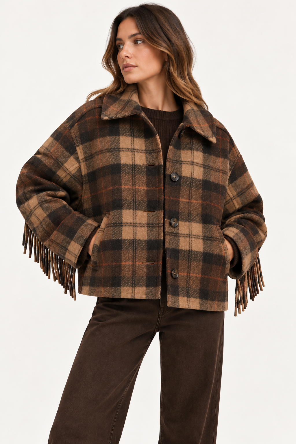 A woman wearing a brown and tan plaid fringed jacket with a collar, paired with dark brown pants, photographed against a clean white studio background.