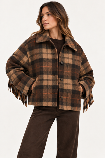 A woman wearing a brown and tan plaid fringed jacket with a collar, paired with dark brown pants, photographed against a clean white studio background.