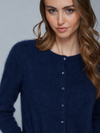 A close-up of a woman wearing a fuzzy navy blue button-front cardigan sweater against a plain light gray studio background.