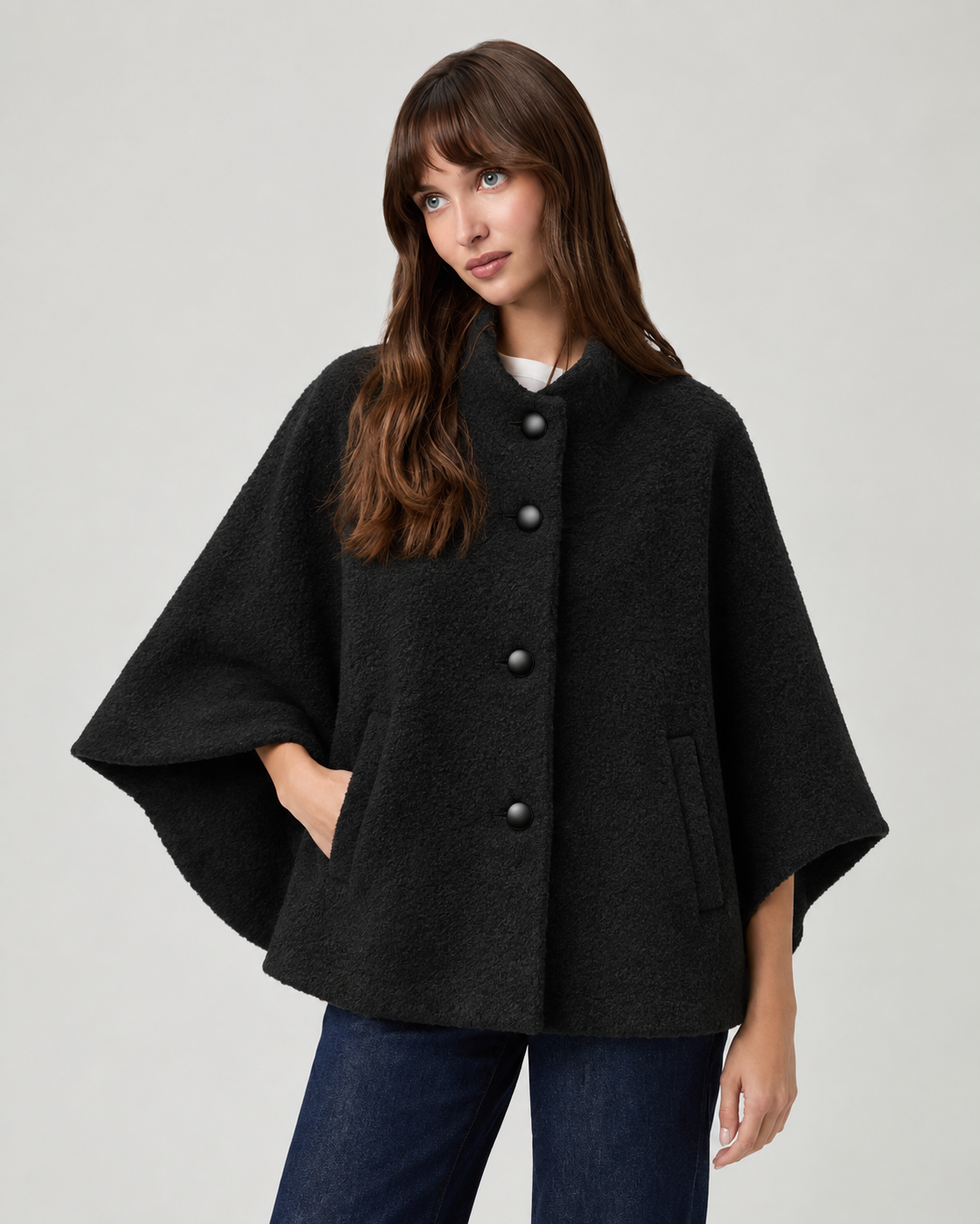 model wearing black cape style coat with blue denim jeans and black boots on a plain white background