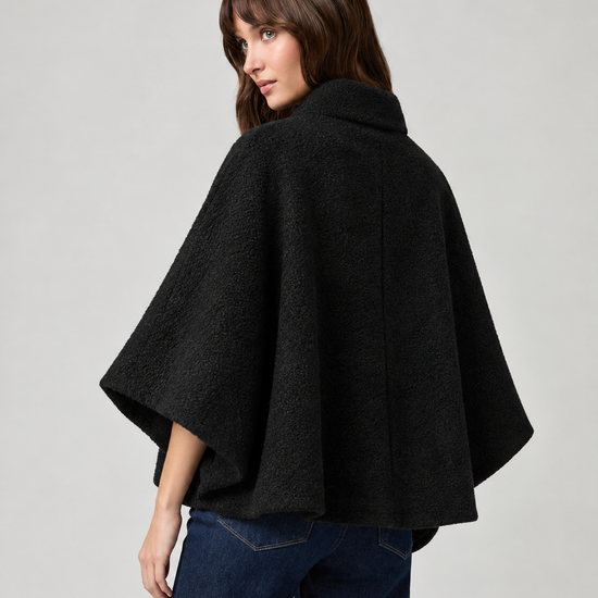 model wearing black cape style coat with blue denim jeans and black boots on a plain white background