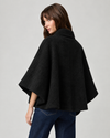 model wearing black cape style coat with blue denim jeans and black boots on a plain white background