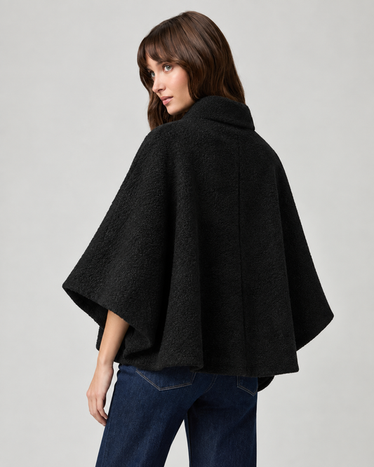 model wearing black cape style coat with blue denim jeans and black boots on a plain white background