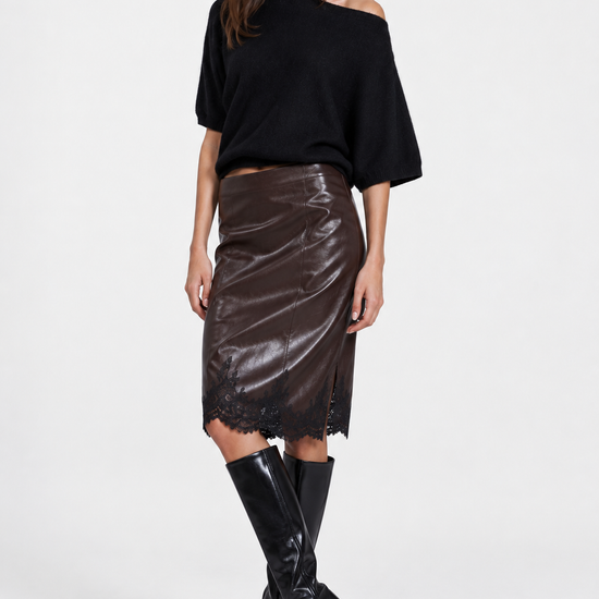 A model wearing a black off-the-shoulder knit top, a shiny dark brown faux-leather midi skirt, and black knee-high boots, posed against a light gray studio background.