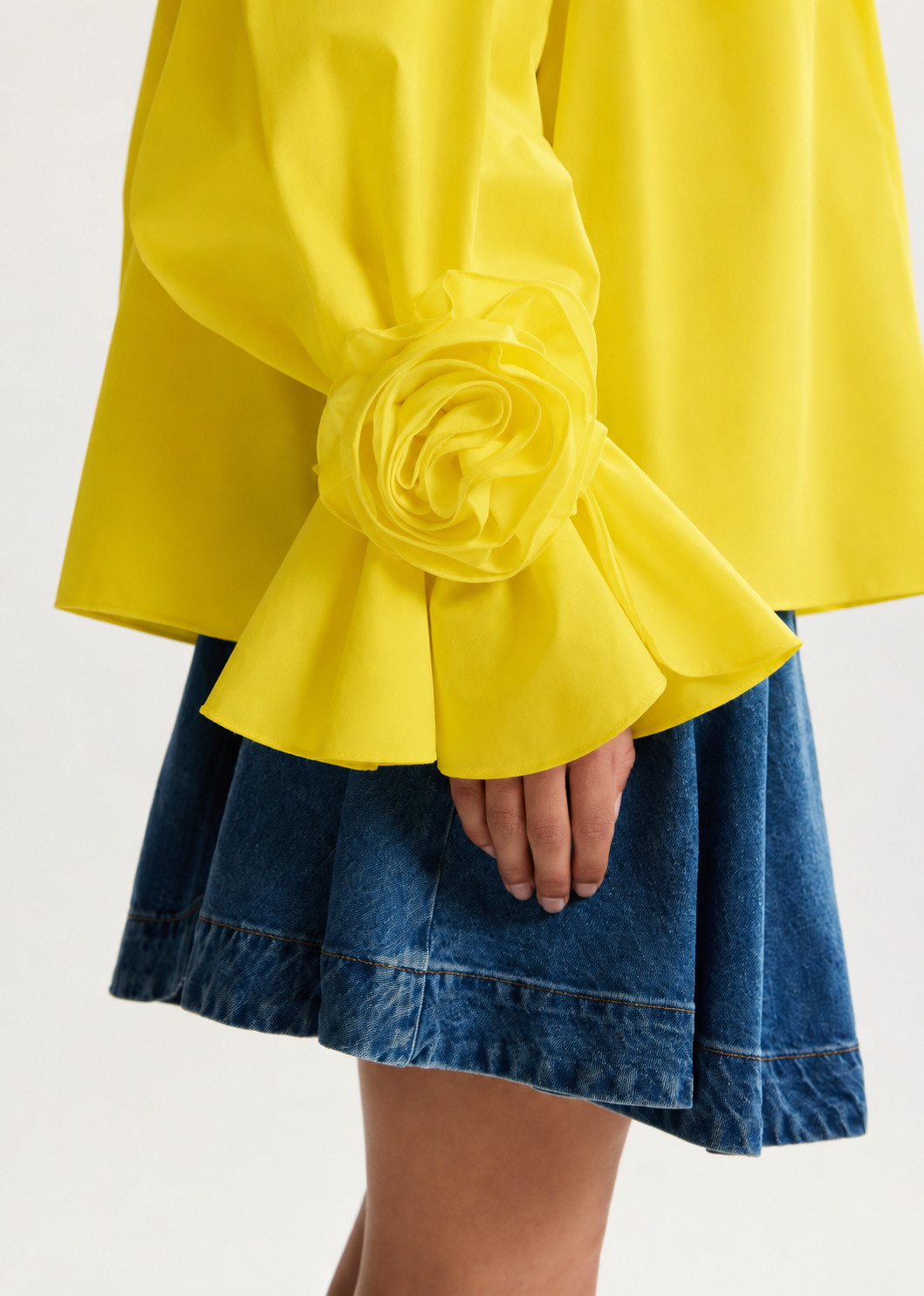 Yellow blouse with ruffled sleeves and a blue denim skirt on a white background