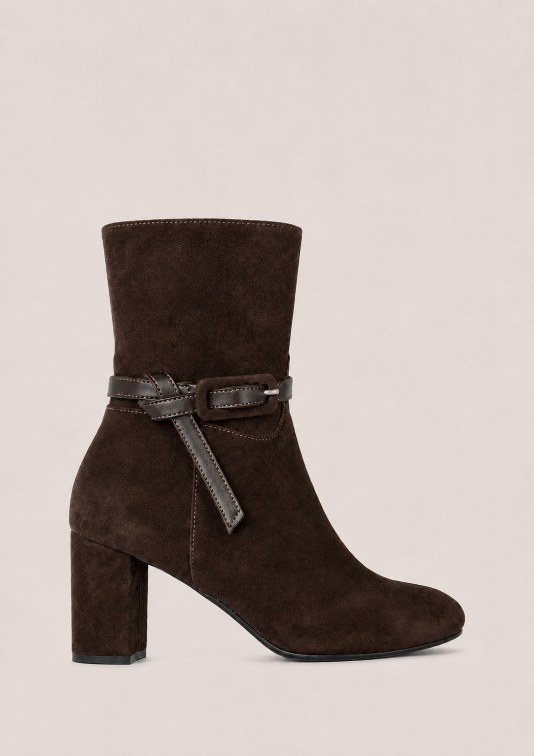 A dark brown suede ankle boot with a block heel and a matching dark brown leather strap detail around the ankle, shown against a solid light beige background.