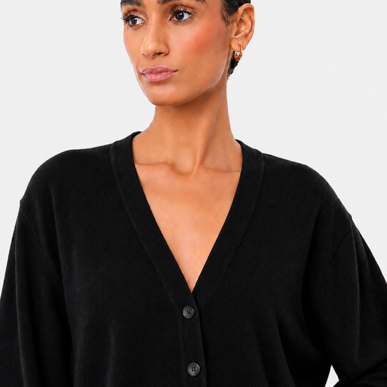 A woman wearing a black long-sleeve V-neck button-up cardigan sweater, shown from the chest up against a light gray studio background.