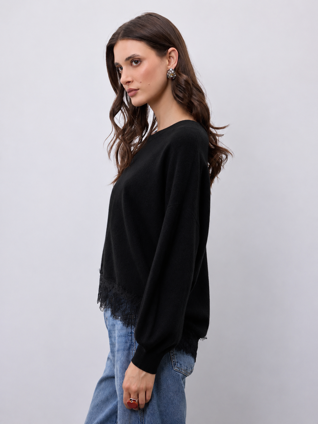 model wearing a black crew neckline knit with lace hem and blue jeans 