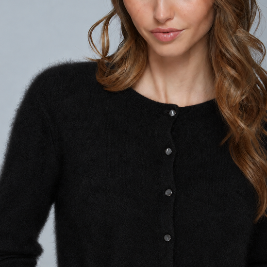 A close-up of a woman wearing a black fuzzy button-front cardigan sweater against a light gray studio background.