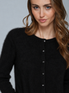 A close-up of a woman wearing a black fuzzy button-front cardigan sweater against a light gray studio background.