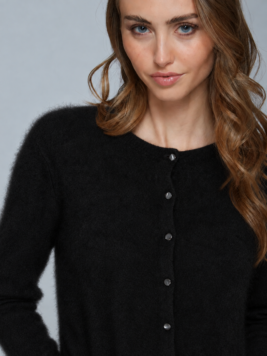 A close-up of a woman wearing a black fuzzy button-front cardigan sweater against a light gray studio background.